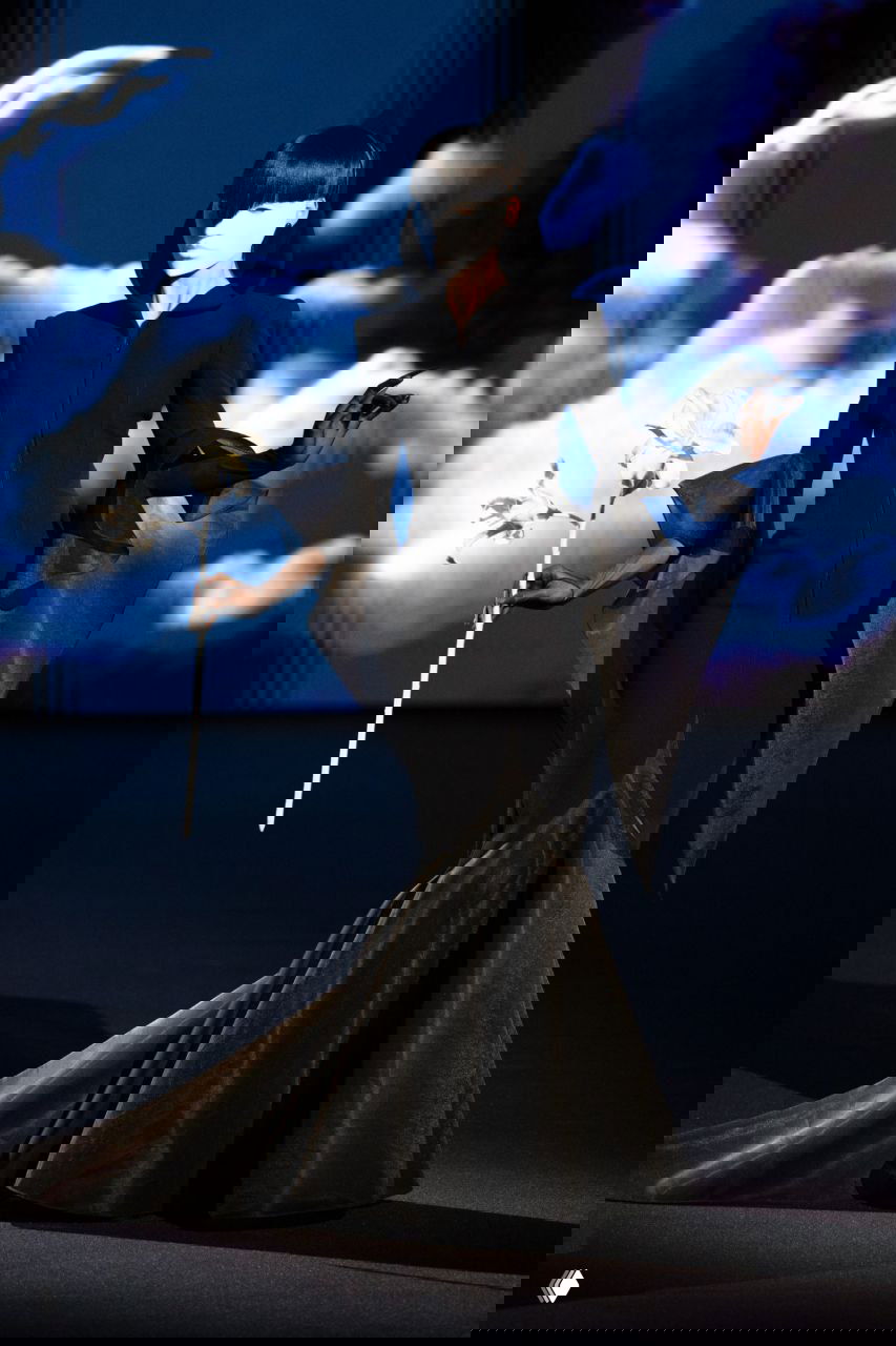 Элегантное чёрное платье с длинным шлейфом и маской, модель держит цветок — театральный образ из кутюрной презентации Роберта Вуна.