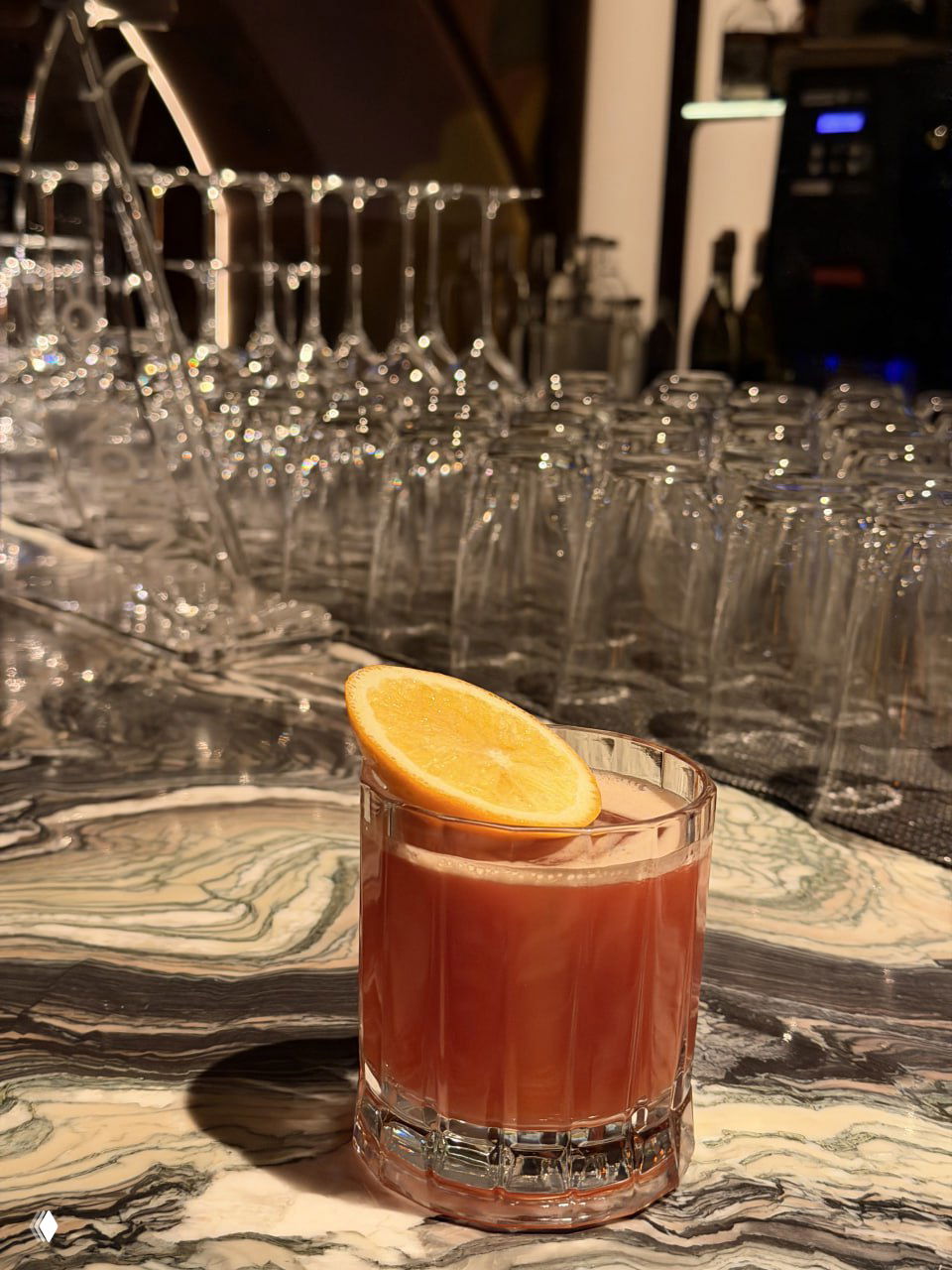 Крупный план стакана с коктейлем KhromRocks на мраморной стойке: апельсиновая долька сверху, коралловый цвет напитка