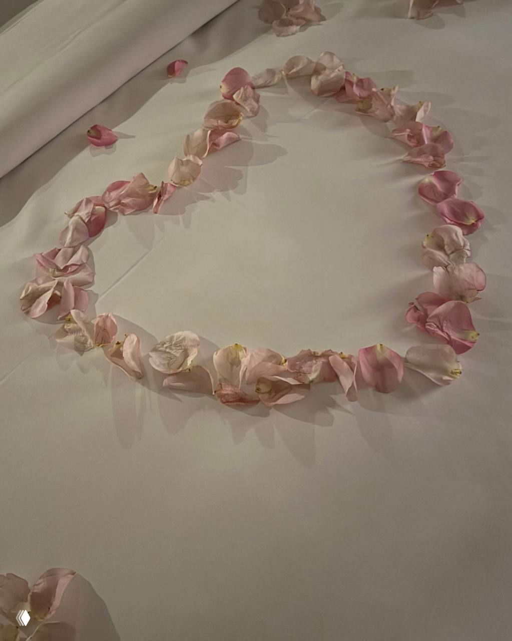 Сердце из розовых лепестков, выложенное на светлом постельном белье, романтическая декорация в честь юбилейной даты пары.