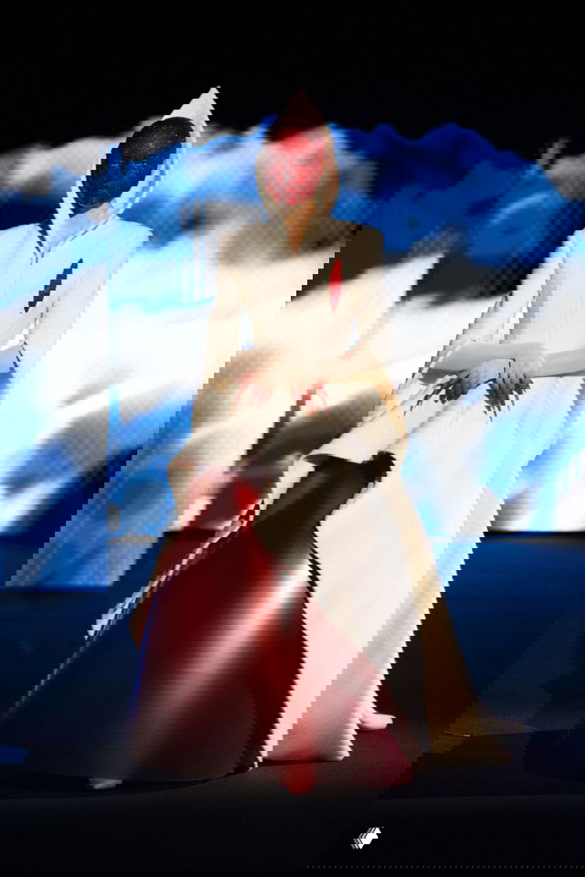 Белое архитектурное платье с капюшоном и красной маской на лице модели: сочетание скульптурности и цветового контраста в коллекции Роберта Вуна.