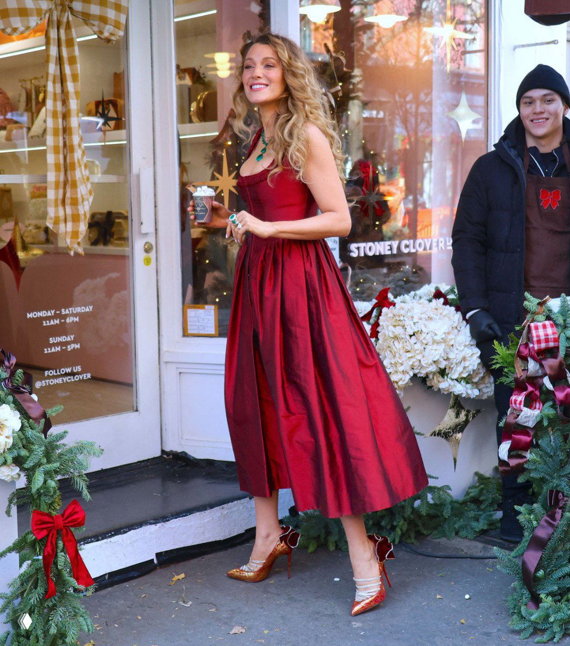 Блейк Лайвли у входа в Stoney Clover Lane в красном платье, в руках кофе, окружённая цветочной и рождественской декорацией и украшениями Lorraine Schwartz.