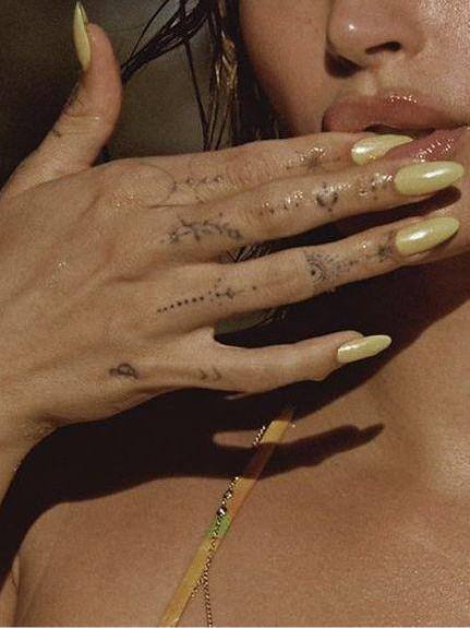 Руки с пастельно-желтым маникюром и татуировками на коже; снимок с влажным эффектом кожи, акцент на текстуру лака и длину ногтей.
