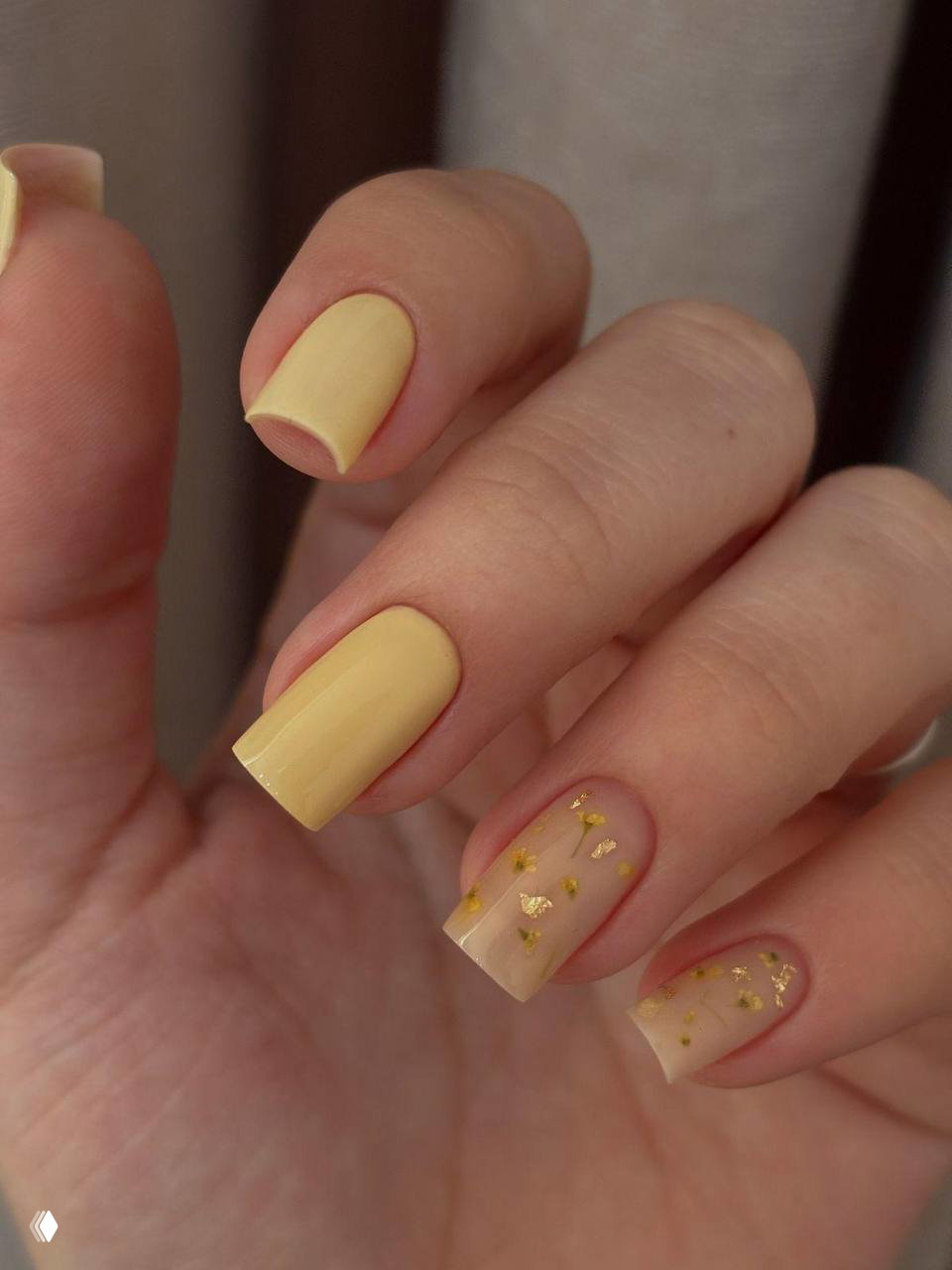 Крупный план матового желтого маникюра на средней длине с акцентом на декорированные прозрачные ногти и золотые вкрапления.