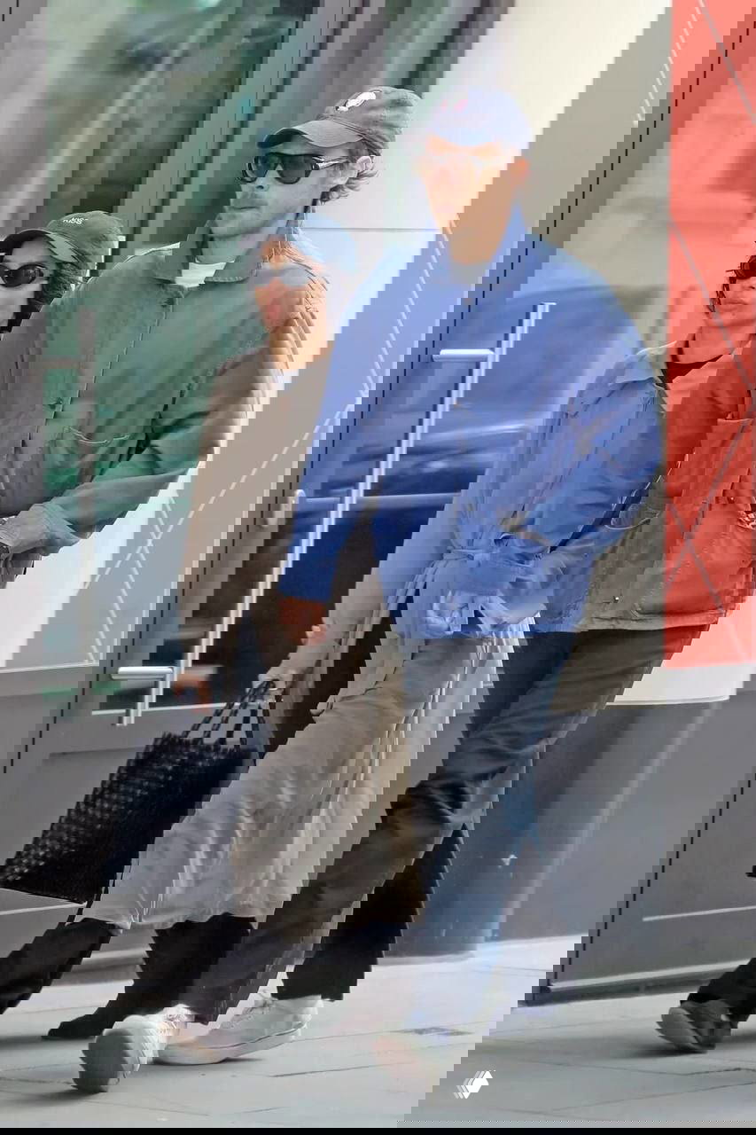 Двое идут по тротуару держась за руки: женщина в пальто и мужчина в синей куртке — папарацци запечатлели прогулку по городу.