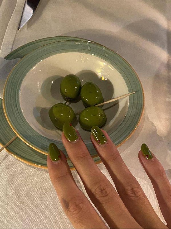 Ногти средней длины, покрытые приглушенным оливковым лаком, фотография в интерьере с блюдом оливок — гармония цвета и контекста.