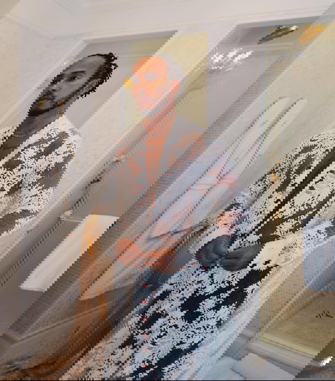 Льюис Хэмилтон в ажурной белой кружевной рубашке в интерьере; пример его склонности к «женственным» тканям и фактурам в образах.