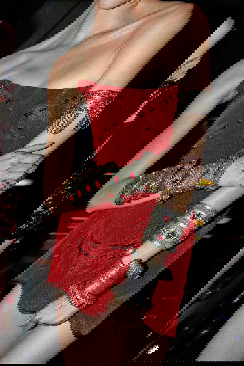 Модель в красном корсете и несколько массивных металлических браслетов с декоративными вставками — акцент на королевской, богатой эстетике украшений.