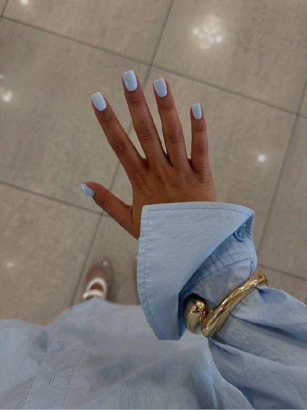 Отдаленный снимок руки с пастельно-голубым маникюром; светлый наряд и отражения пола создают чистый, опрятный визуал.