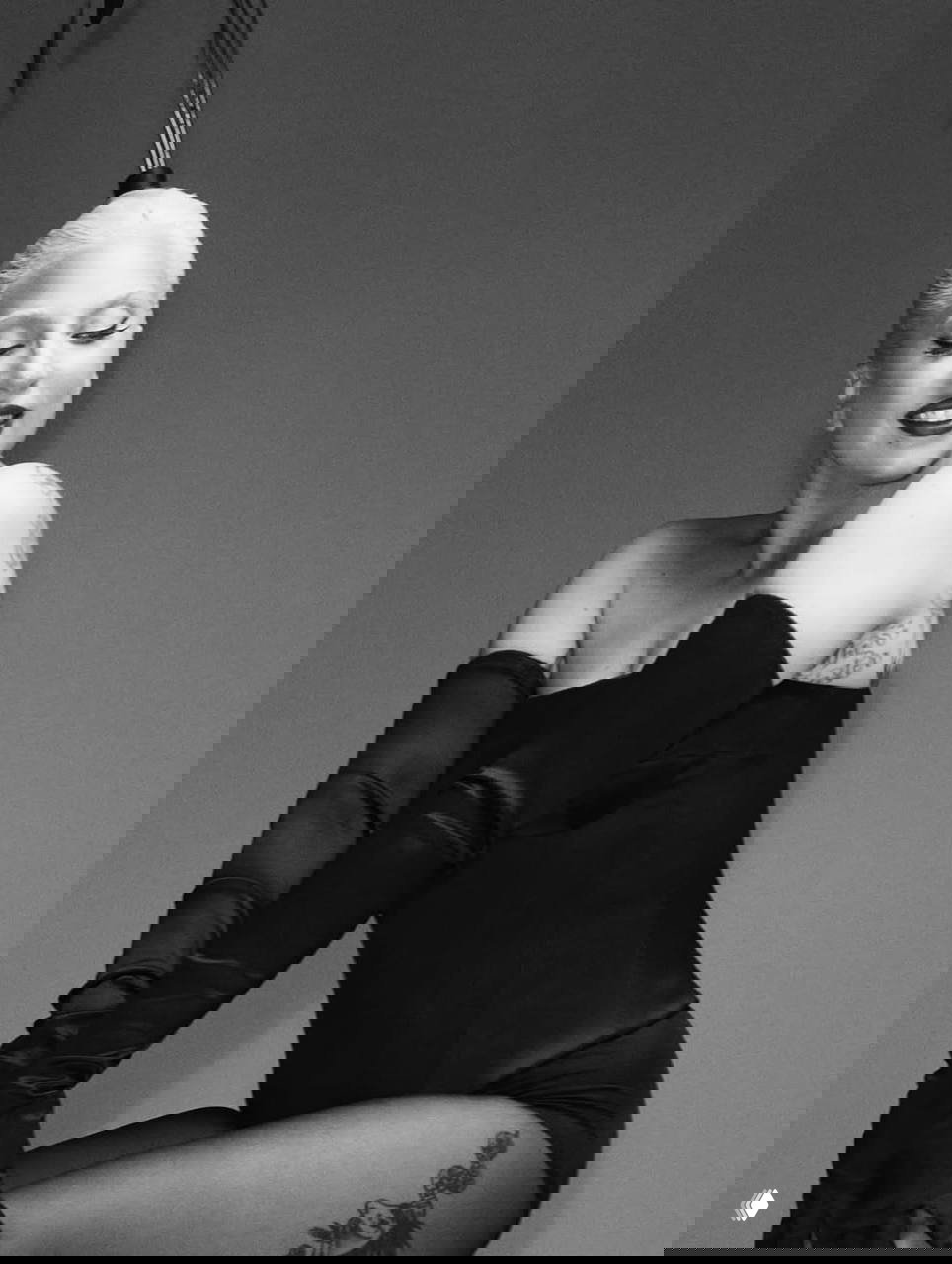 Чёрно‑белая студийная фотография: женщина в боди и длинных перчатках, улыбается, видны татуировки на руке и элегантная постановка позы.