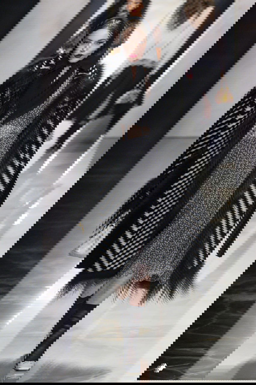 Модель в длинном полосатом меховом пальто и полупрозрачном кружевном платье идёт по подиуму Dolce & Gabbana 2026/27.