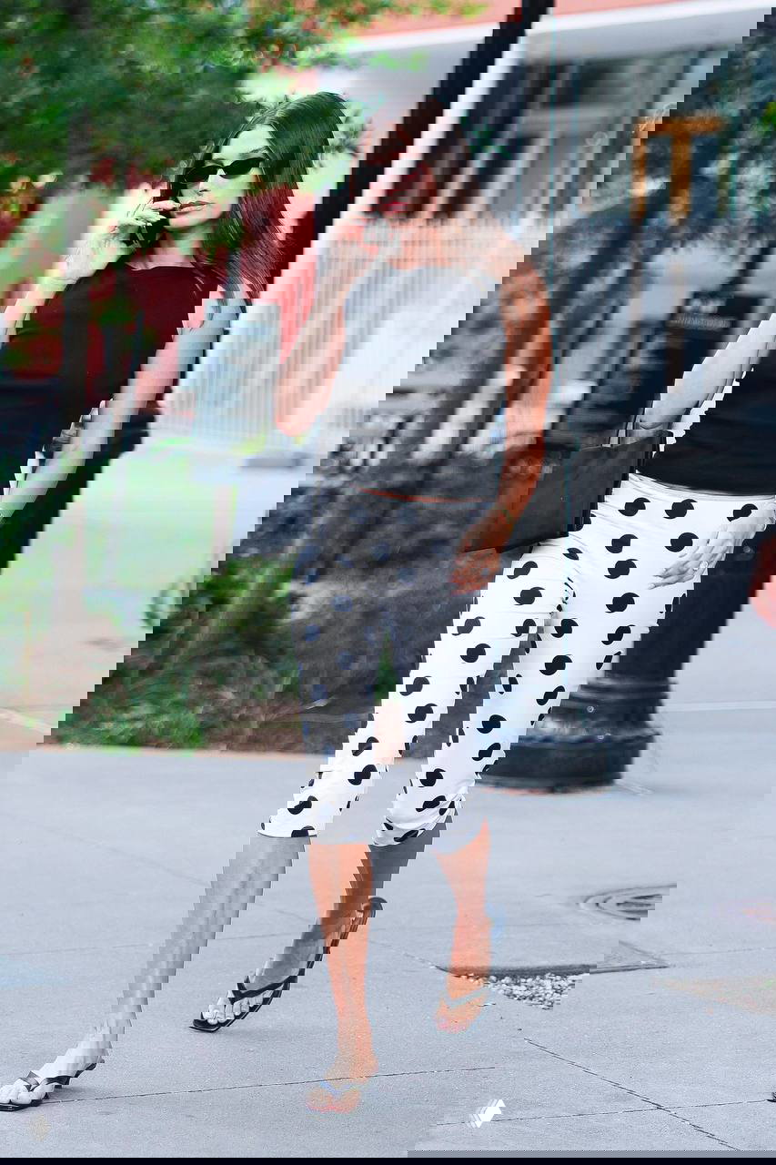 Уличный снимок модели в укороченных гороховых брюках и черном топе, городской летний образ с минималистичной сумкой и мюлями.