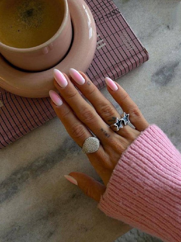 Крупный план рук с лилово-голубым пастельным маникюром на короткой длине; светлый интерьер и кольцо на пальце создают элегантный образ.