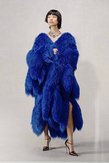 Модель в пышной синей шубе и заметным ожерельем — театральный, роскошный образ с акцентом на крупные украшения.