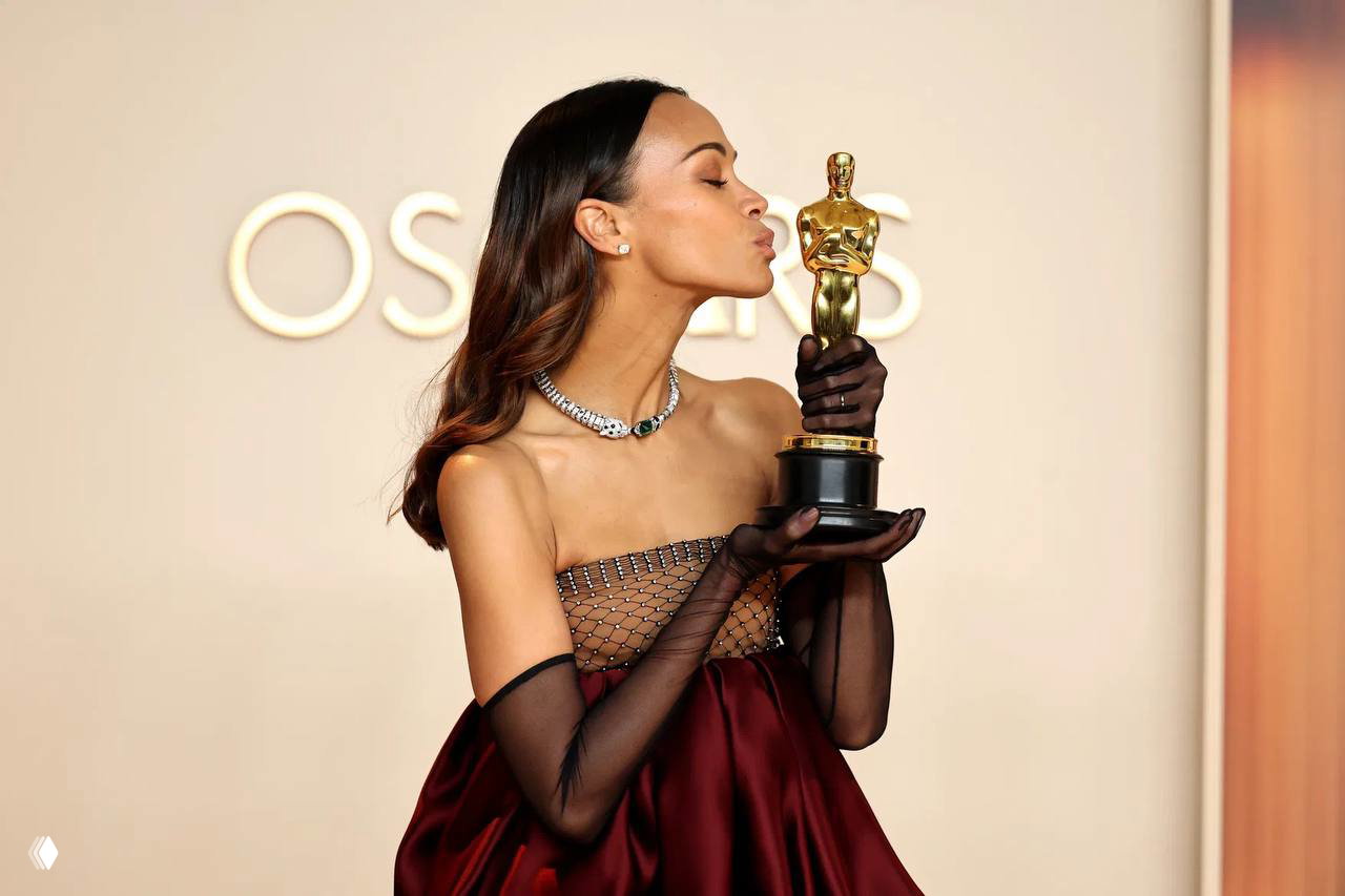 Женщина в вечернем платье целует статуэтку премии, съемка на светлом фоне с элементами глянцевого кадра и атмосферой наградного события.