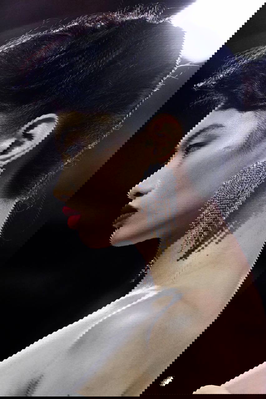 Крупный план профиля модели с длинной висячей серьгой, сверкающей и драматичной — пример декора в королевском стиле на лице.