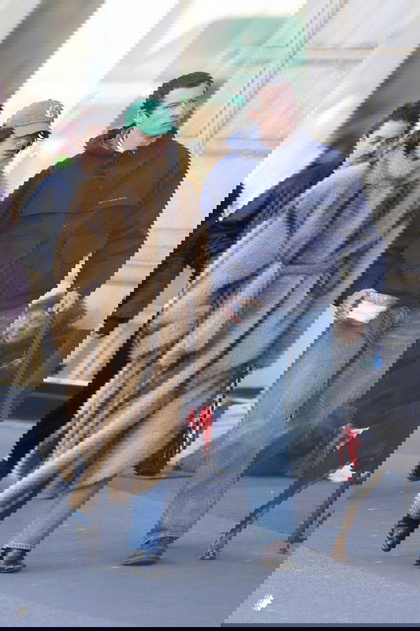 Дуэт на прогулке: женщина в крупном меховом пальто и мужчина в темной куртке, уличная сцена, пешеходный поток на заднем плане.