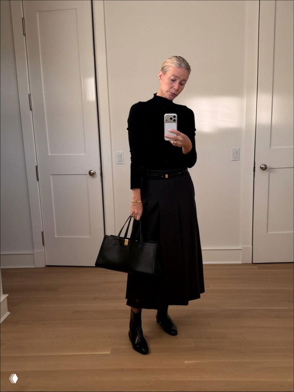 Гвинет Пэлтроу позирует в длинной тёмной юбке, чёрном свитере и кожаной сумке, образ подчеркнут строгой элегантностью и минималистичным кроем