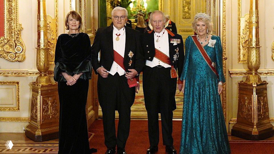 Групповой снимок гостей и членов королевской семьи в парадной обстановке зала с золотым декором и красными коврами.