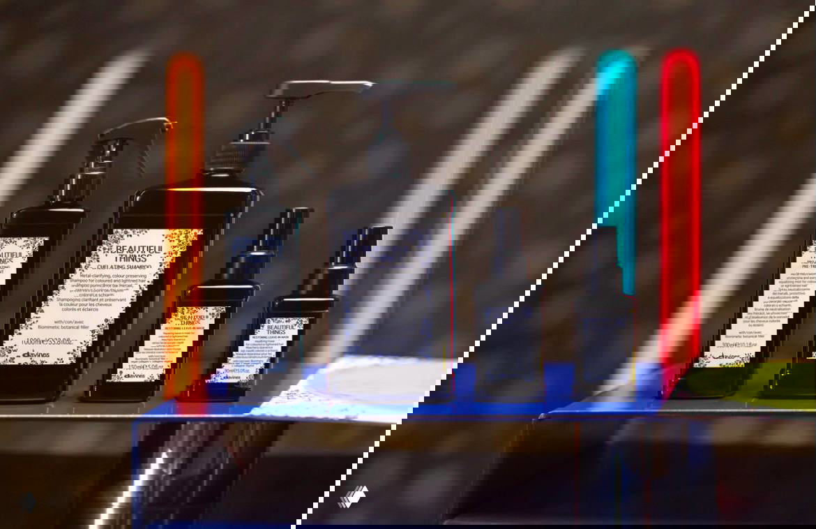 Набор средств Davines Beautiful Things на подиуме: флаконы и диспенсеры для салонного детокс-сервиса, снятые на тёплом фоне с цветными неоновыми акцентами.