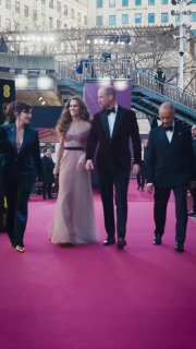 Пара на красной дорожке в длинных вечерних нарядах идёт по ковровой дорожке у входа на церемонию BAFTA, вертикальный кадр