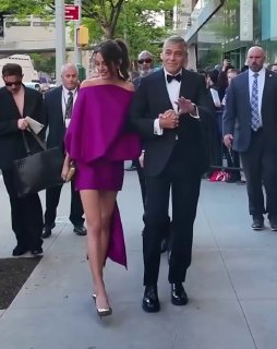 Джордж и Амаль идут по тротуару у входа: он в смокинге, она в мини-платье фуксии, вокруг люди и охрана.