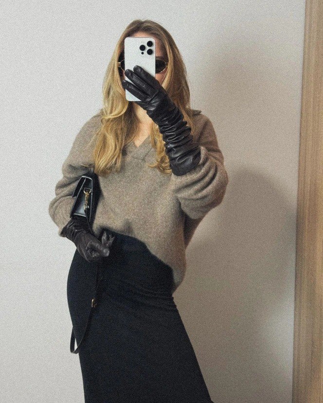 Селфи в зеркале: женщина держит iPhone и демонстрирует чёрные длинные кожаные перчатки в сочетании с уютным свитером и юбкой.