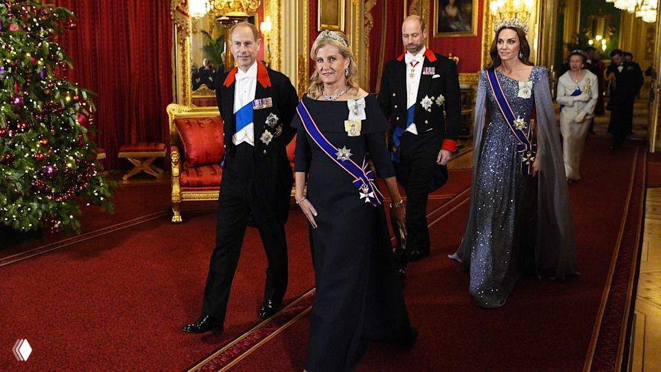 Проход гостей по украшенному коридору рядом с рождественской ёлкой и золочёными аксессуарами интерьера замка.