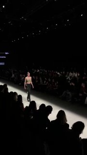 Модель в спортивном образе проходит показывать коллекцию; тёмный зал и пунктирные источники света создают драматичный эффект подиума.