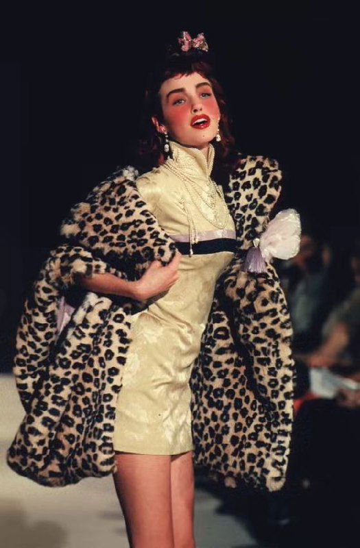 Модель в леопардовой шубе и коротком платье на подиуме Dior 1998, динамичная поза, выразительный макияж и игривый дух показа в кадре.