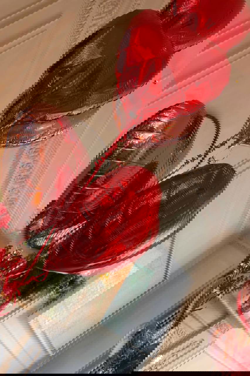 Крупный план красных и розовых сердцевидных фольгированных шаров на фоне лепнины и потолочных украшений в интерьере дома.