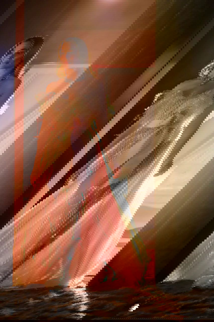 Актриса в полупрозрачном розовом платье с большим бантом и сияющей текстурой ткани, контровой свет подчеркивает переливы материала.