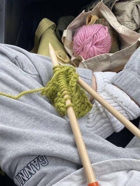 Руки в тёплой одежде вяжут зелёную пряжу на крупных деревянных спицах; рядом сумка с мотком — уютный творческий момент.