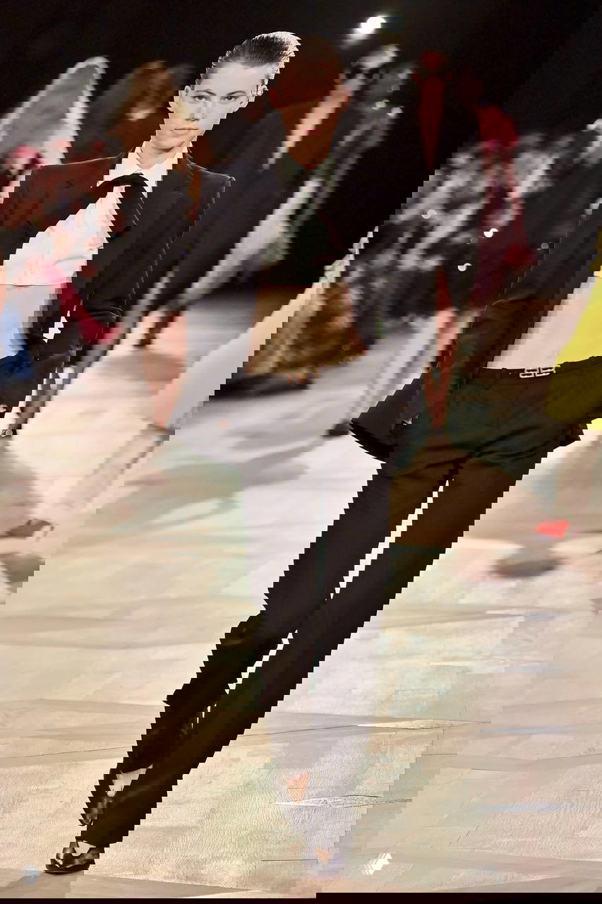 Подиумный выход: модель в приталенном костюме с открытой талией и строгим кроем демонстрирует направление к более собранным, кутюрным силуэтам на показе.