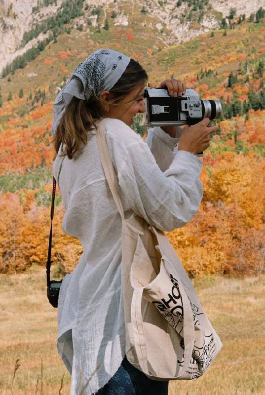 Девушка на фоне осенних холмов фотографирует на плёночную камеру: походная визуальная практика и интерес к аналоговой фотографии.