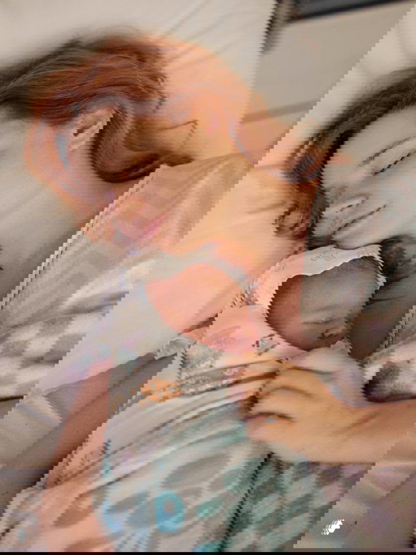 Мила Ершова отдыхает в палате с новорождённым сыном Каем, завернутым в плед: спокойный постродовый кадр матери с малышом на груди.