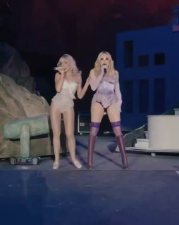 Дуэт Мадонны и Сабрины Карпентер на сцене Coachella: обе в сценических образах поют рядом у декораций фестиваля в сумеречном свете.