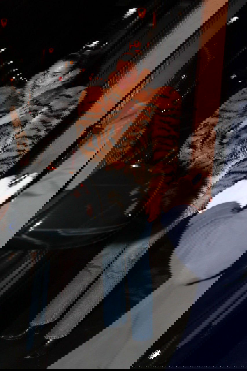 Женщина в эффектной шубе с рисунком «тигр», джинсах и туфлях на улице вечером, снимок папарацци с фокусом на верхнюю одежду.