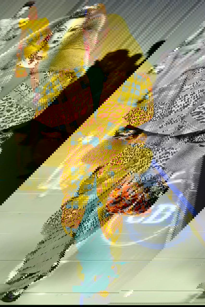 Жёлто-клетчатое пальто с леопардовыми вставками и большим меховым воротником, под которым видна бирюзовая драпировка платья.