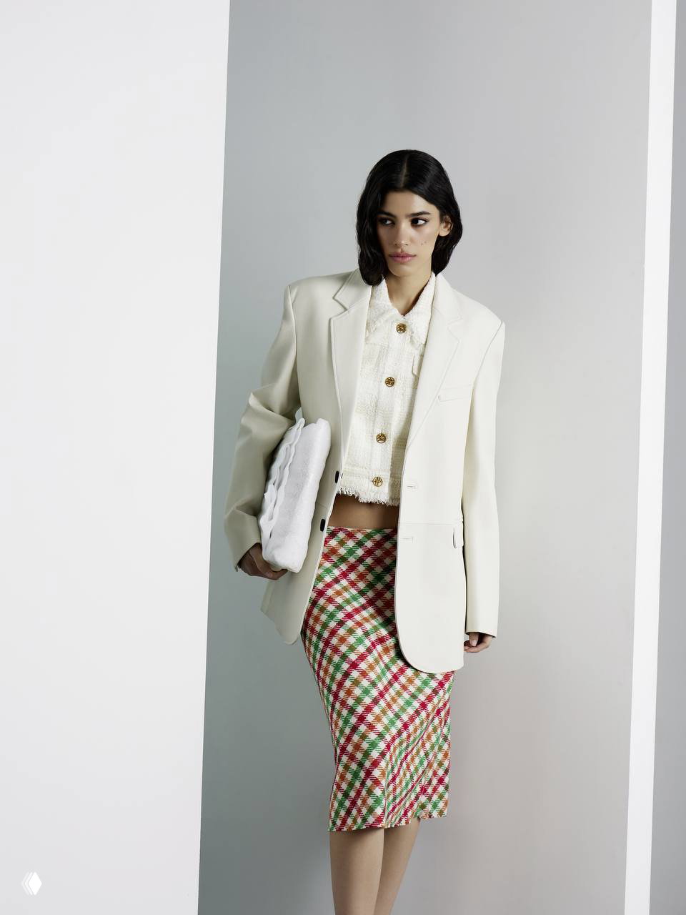 Портретная фотография модели в белом жакете и клетчатой юбке на нейтральном фоне студии, акцент на силуэте и текстуре тканей.