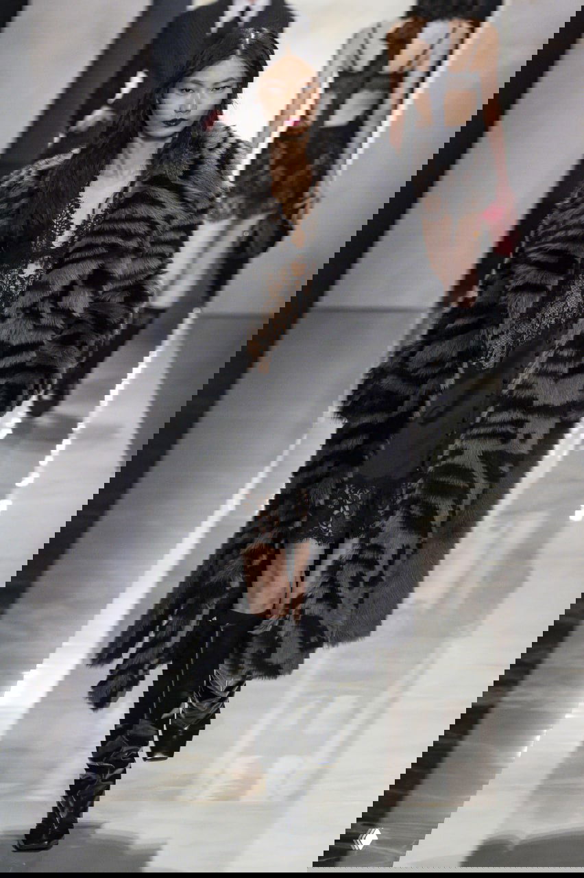 Модель в чёрной кружевной комбинации и массивной шубе с графичным принтом идёт по подиуму коллекции Dolce & Gabbana.