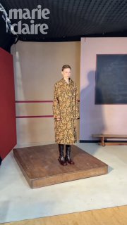 Модель стоит на подиуме-кубике в пальто с цветочным принтом в студийной зоне с нейтральным фоном и мягким освещением съемки.