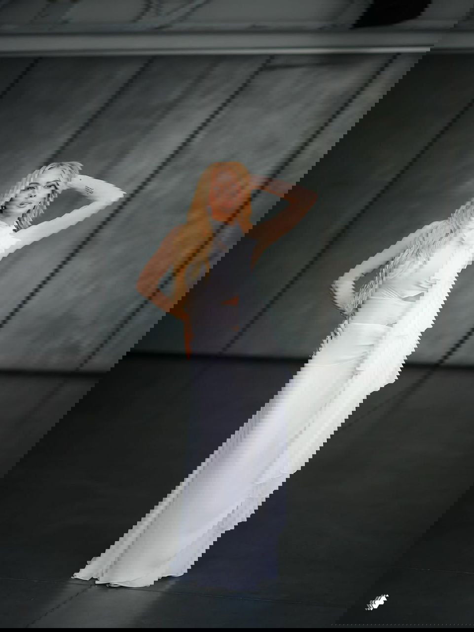 Линдси Лохан в белом длинном платье с драпировкой и крупным бантом у шеи, поза в пол-оборота подчёркивает минимализм и изысканность образа.