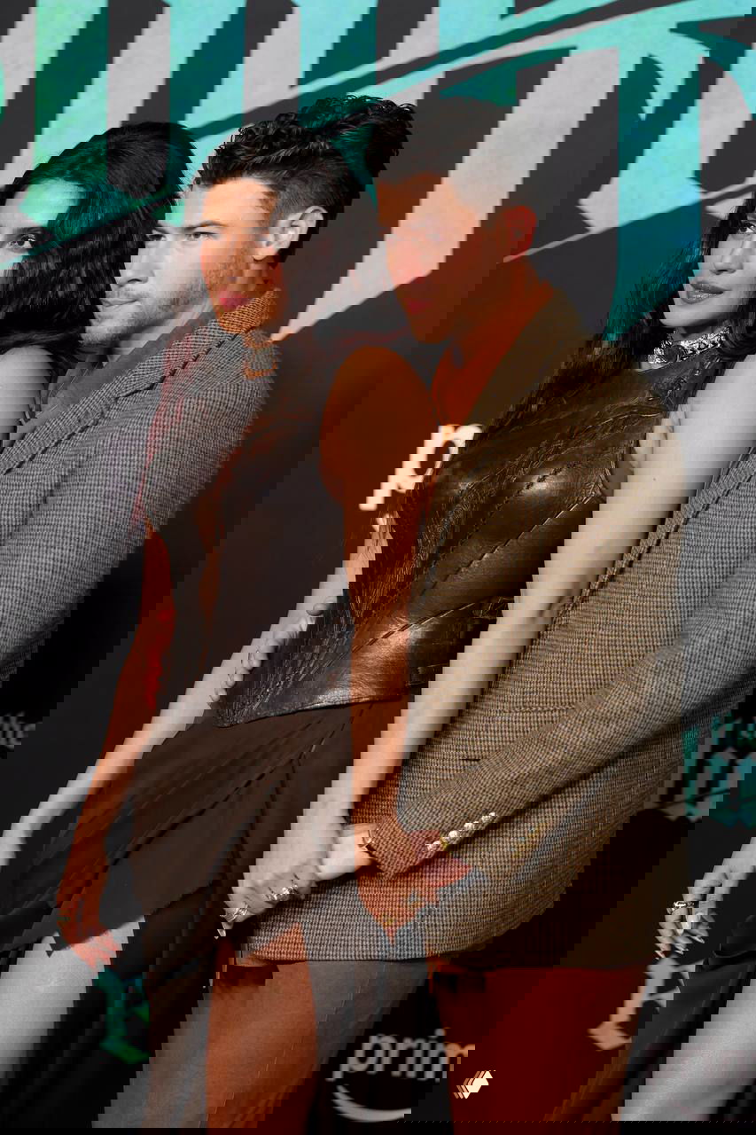 Нежный кадр: Ник держит Приянку за талию, видно высокий разрез и шлейф её платья на фоне логотипа премьеры в Лос‑Анджелесе.