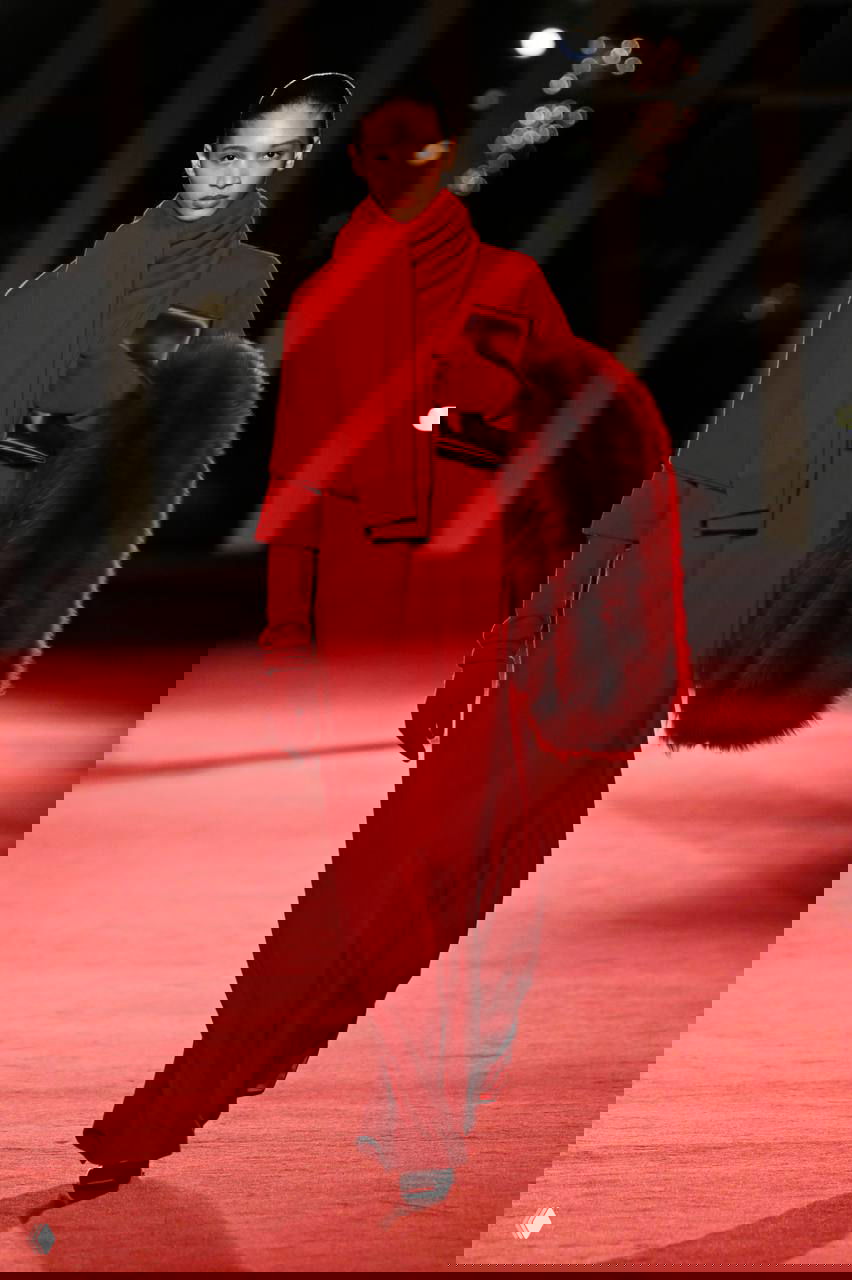 Модель в длинном красном платье с аккуратной накидкой из меха идет по подиуму Michael Kors, оттеняя насыщенные оттенки и фактуры коллекции.