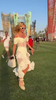 Посетительница фестиваля в белом летящем платье идёт по газону на фоне ярких арт-инсталляций и солнечного неба летнего дня.