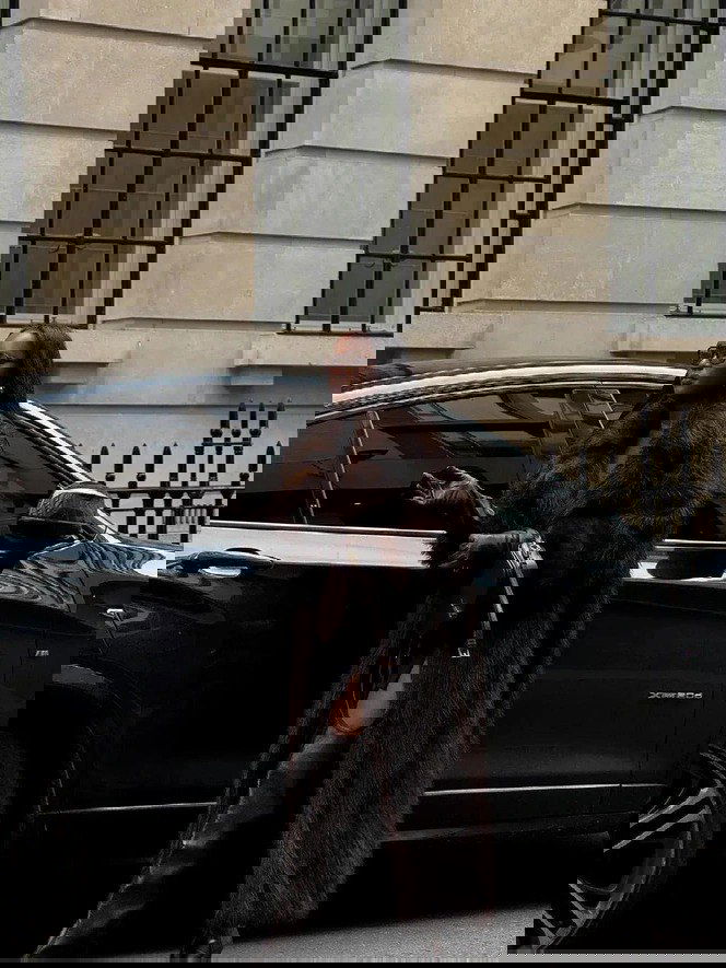 Высокая длинная тёмная шуба в пол на модели возле автомобиля, образ с высокими сапогами и аксессуарами, выглядит очень элегантно