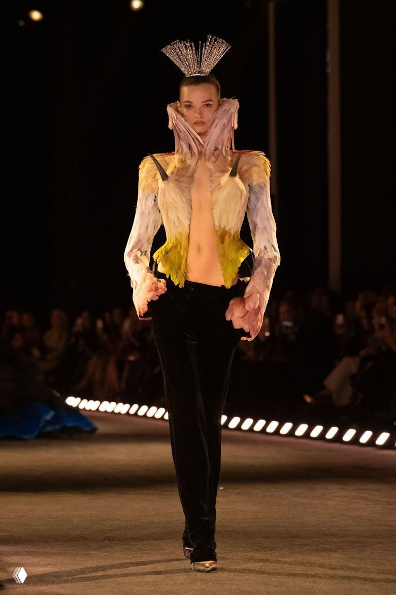 Модель в жакете, украшенном пастельными перьями и короноподобным аксессуаром, высокая мода с театральными элементами на показе Schiaparelli.