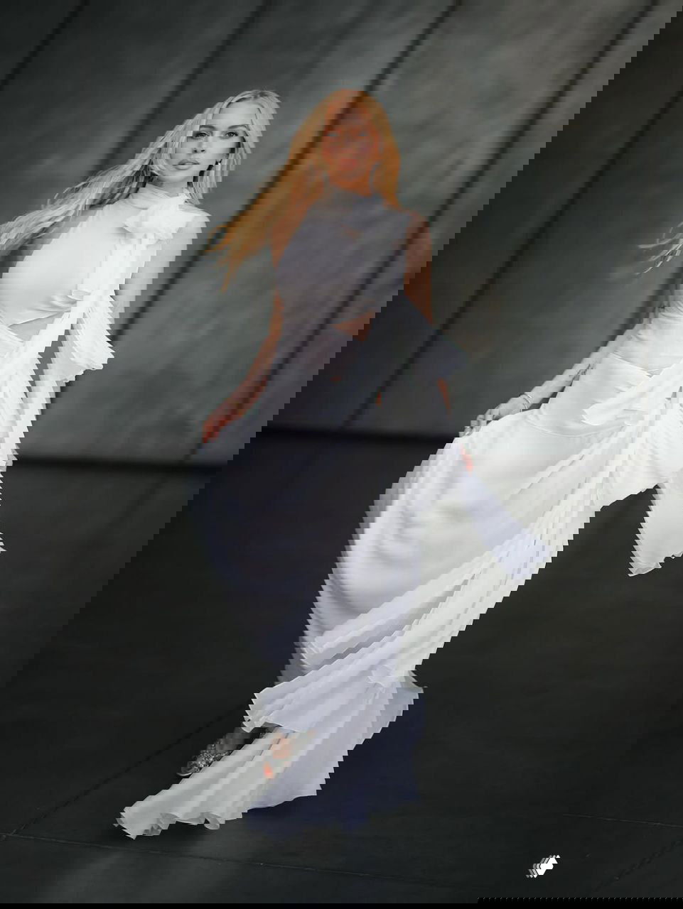 Линдси Лохан в динамичном кадре: белое платье с развевающимися складками, движение ткани и элегантность на строгом индустриальном фоне.