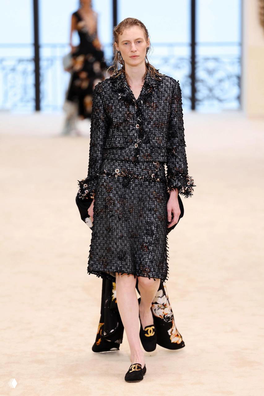 Модель в твидовом жакете и юбке с фирменной бахромой Chanel, классический лук твида на современной неделе моды.