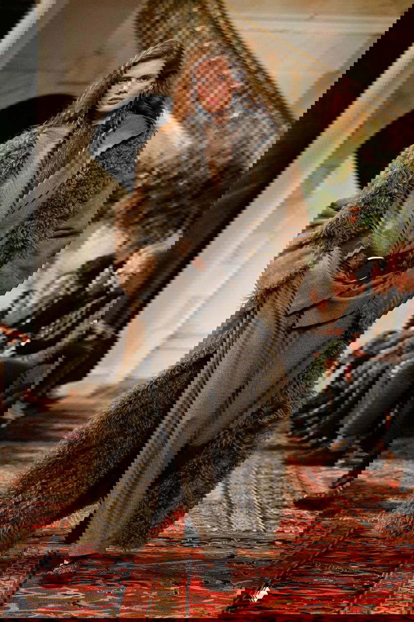 Модель в длинном дублёном пальто с пушистыми вставками и широким ремнём, свободные брюки и текстурный ковер подиума создают массивный образ.